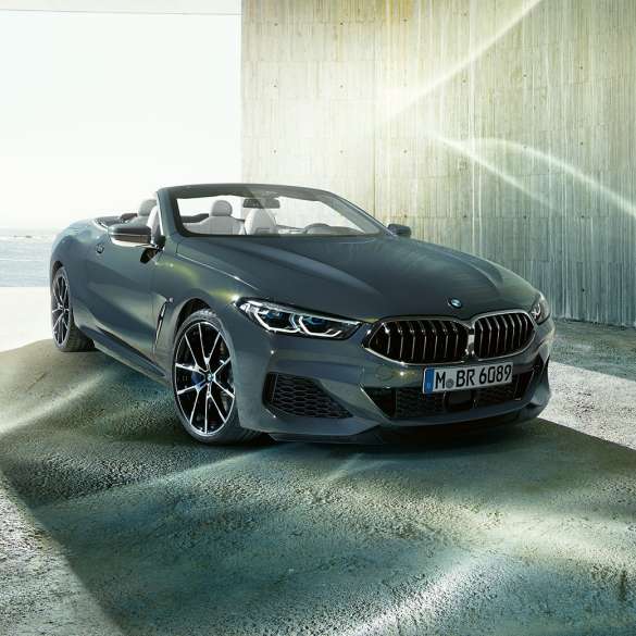 BMW M850i xDrive Cabrio, kolm neljandikku eestvaade. BMW M850i xDrive Cabrio toonis Dravit Grey metallik, avatud pehme katusega, kolm neljandikku eestvaade, seismas ranniku taustal.