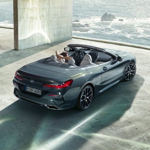 BMW M850i xDrive Cabrio, ülaltvaade. BMW M850i xDrive Cabrio toonis Dravit Grey metallik, avatud pehme katusega, ülaltvaade, parkimas betoonehitise ees ookeani taustal.