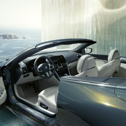 BMW M850i xDrive Cabrio, salong. BMW M850i xDrive Cabrio toonis Dravit Grey metallik, avatud pehme katusega, salong koos nahkkattega M-rooliga ja BMW Individuali nahkpolstriga 'Merino' Ivory White.