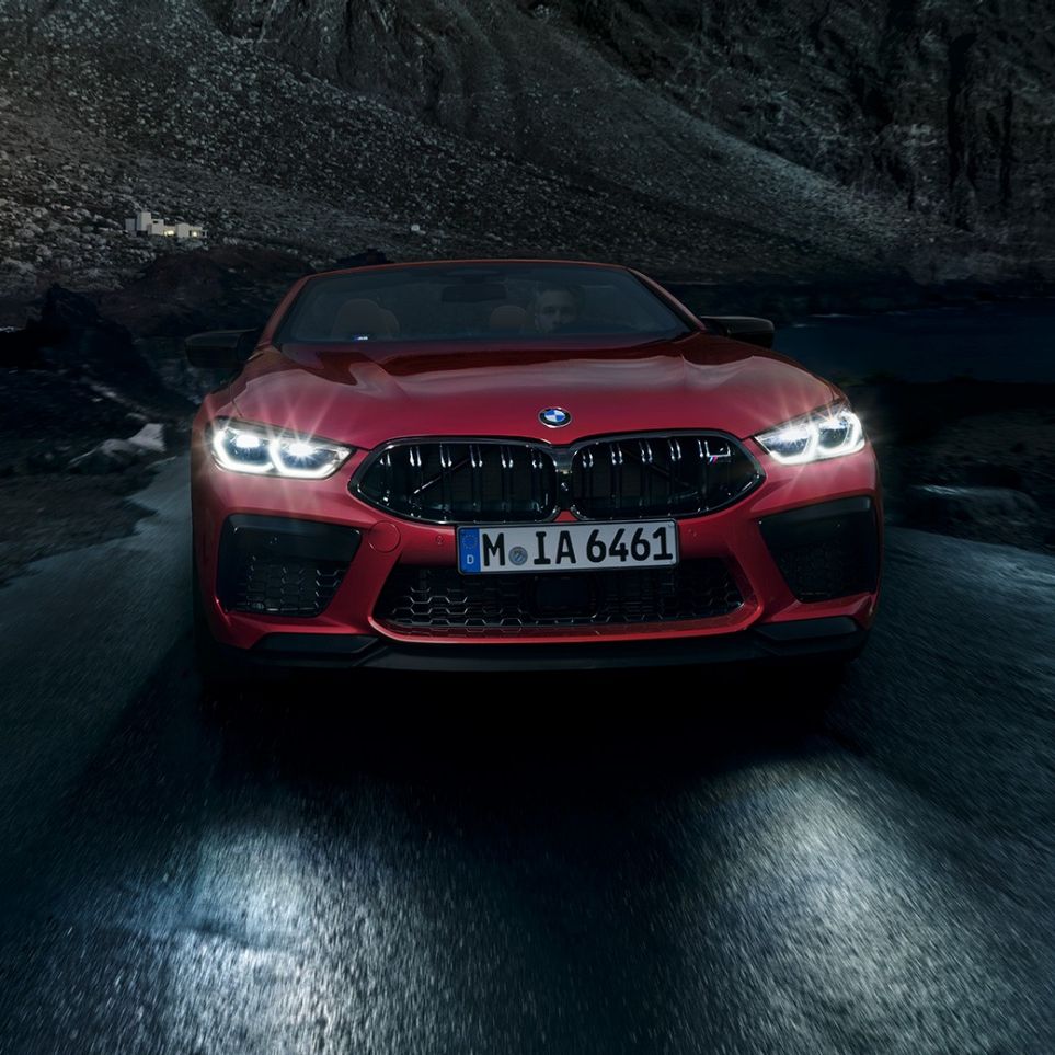 BMW M8 Competition Cabrio, eestvaade. BMW M8 Competition Cabrio toonis Motegi Red metallik, säravate esituledega, eestvaade, öösel sõitmas.