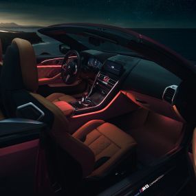 BMW M8 Competition Cabrio, salong. BMW M8 Competition Cabrio, avatud pehme katusega, salong punase salongivalgustusega öösel.
