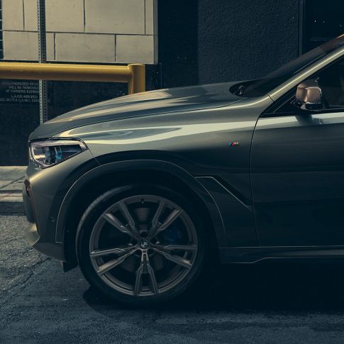BMW X6 M50i külgvaates Mees nõjatumas linnakeskkonnas vastu külgvaates mudelit BMW X6 M50i