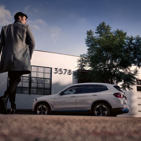BMW iX3 G08 külgvaade hoone ees koos mehega BMW iX3 G08 2020 Mineral White metallik külgvaade hoone ees koos mehega