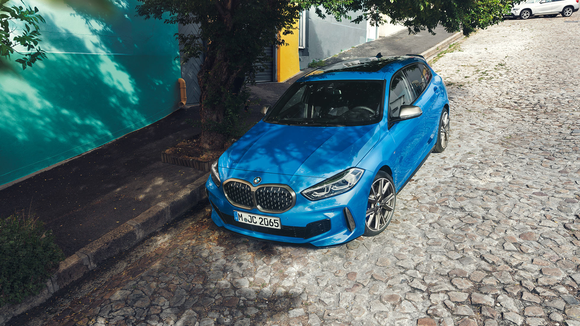1. seeria BMW tee ääres. 1. seeria BMW värvitoonis Misano Blue metallik, kolm neljandiku eestvaade, parkimas tee ääres, ülaltvaates.