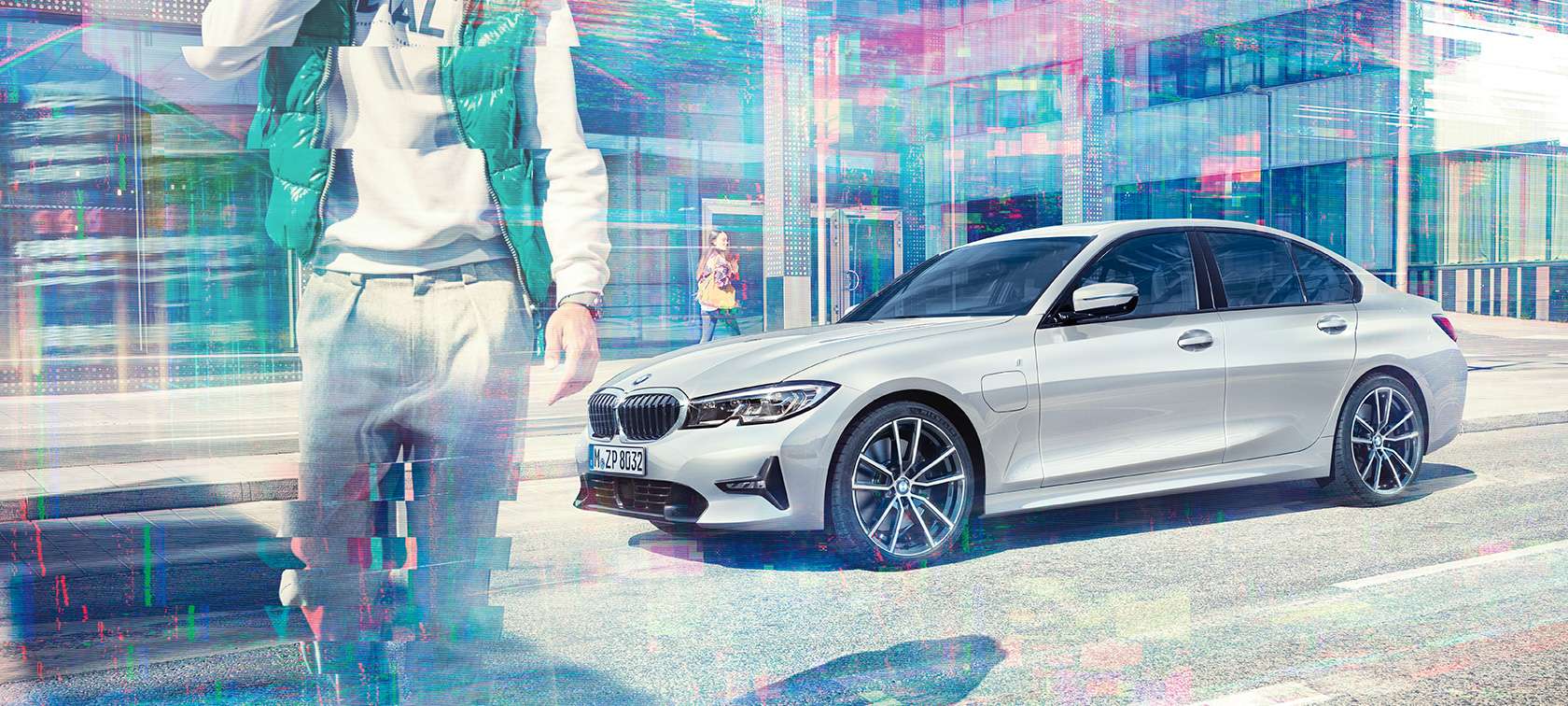 BMW 3. seeria Sedan, BMW 330e külgvaade. BMW 330e Sedan kolm neljandikku külgvaates linna klaashoone taustal koos jalakäijatega.