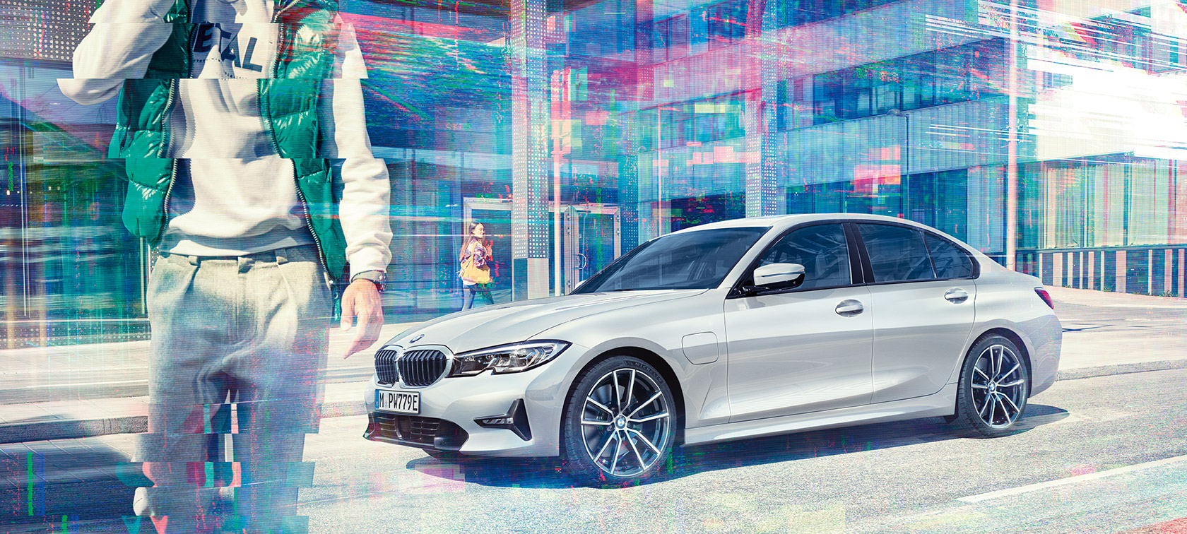 BMW 3. seeria Sedan, BMW 330e külgvaade. BMW 330e Sedan kolm neljandikku külgvaates linna klaashoone taustal koos jalakäijatega.