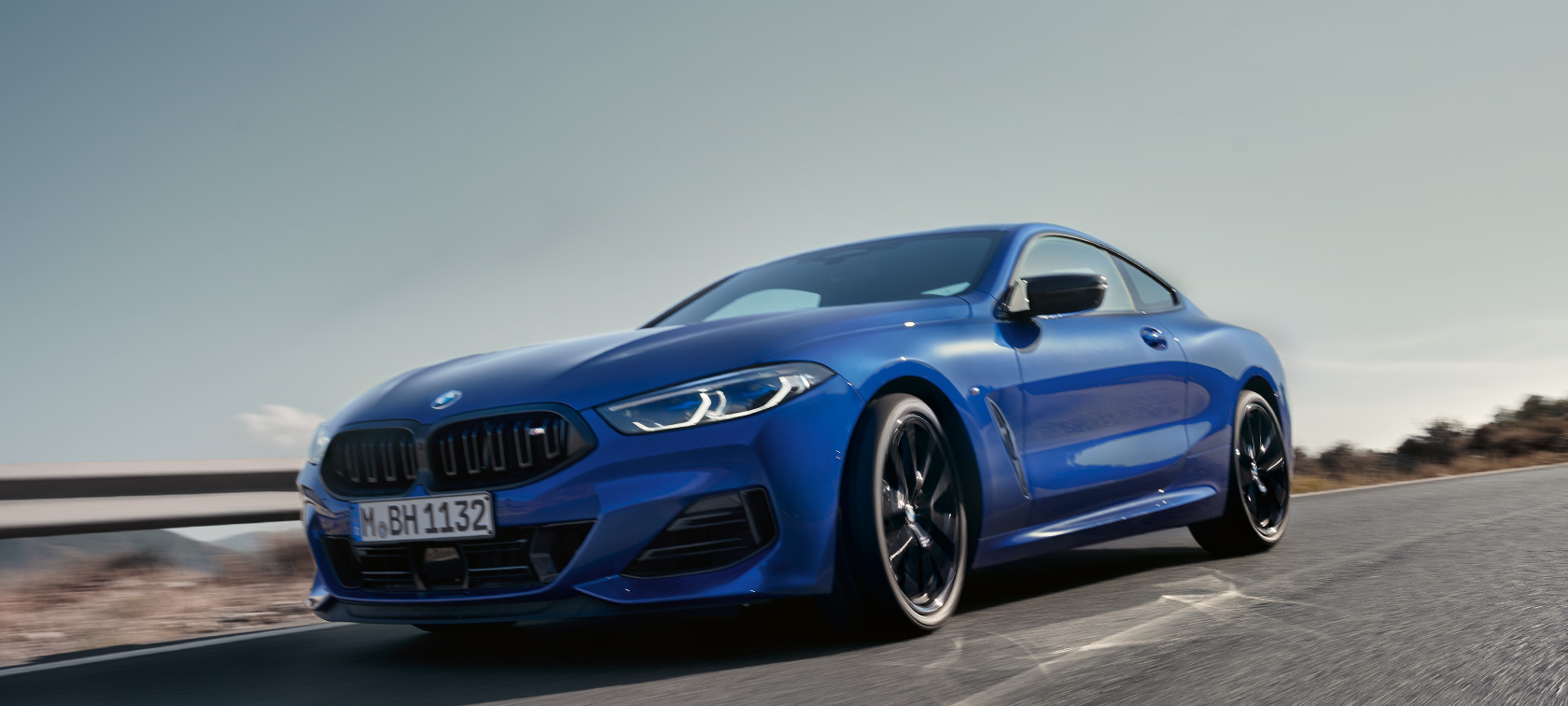 BMW 8. seeria Coupé G15 LCI Facelift 2022 BMW M850i xDrive M Portimao Blue metallik eestvaade madala nurga alt BMW 8. seeria Coupé G15 LCI Facelift 2022 BMW M850i xDrive M Portimao Blue metallik sõitmas maanteel, taustaks mäed, eestvaade madala nurga alt