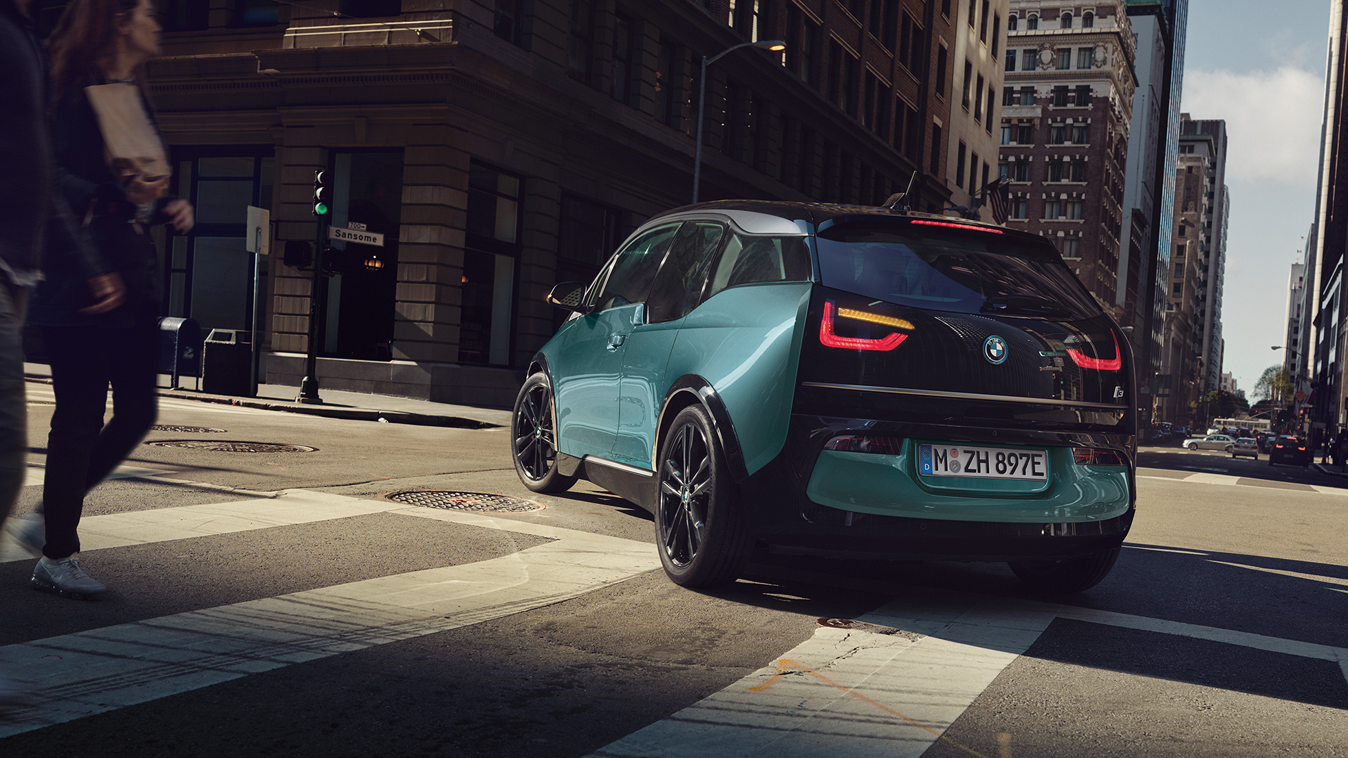 BMW i3 2018, kolm neljandikku tagantvaade sõites BMW i3 I01 2018 Jucaro Beige metallikvärv koos Frozen Grey metallikviimistlusega, kolm neljandikku tagantvaade, sõites linnas