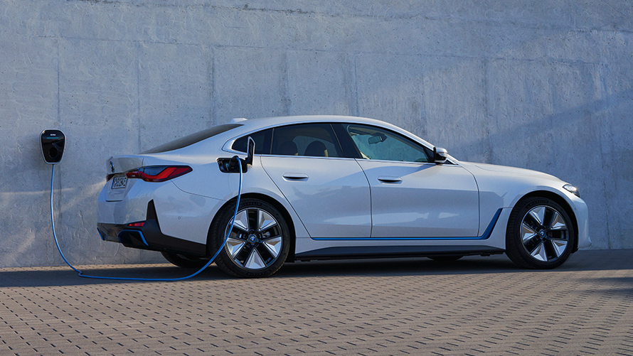Külgvaade koos BMW Wallboxiga, BMW i4 eDrive40 G26 2021 BMW i4 eDrive40 G26 2021 toonis Mineral White, külgvaade, maja ees, mille seinal on BMW Wallboxi laadimisjaam