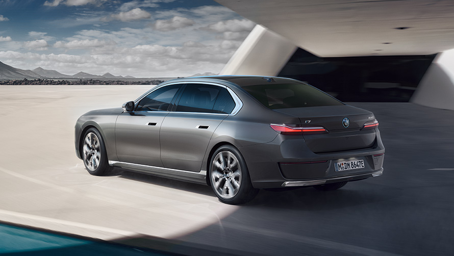 BMW i7 Sedaan G70 BMW Individual Oxid Grey metallik, kolm neljandikku tagantvaade hoone ees seistes BMW i7 Sedaani pakett, kolm neljandikku tagantvaade