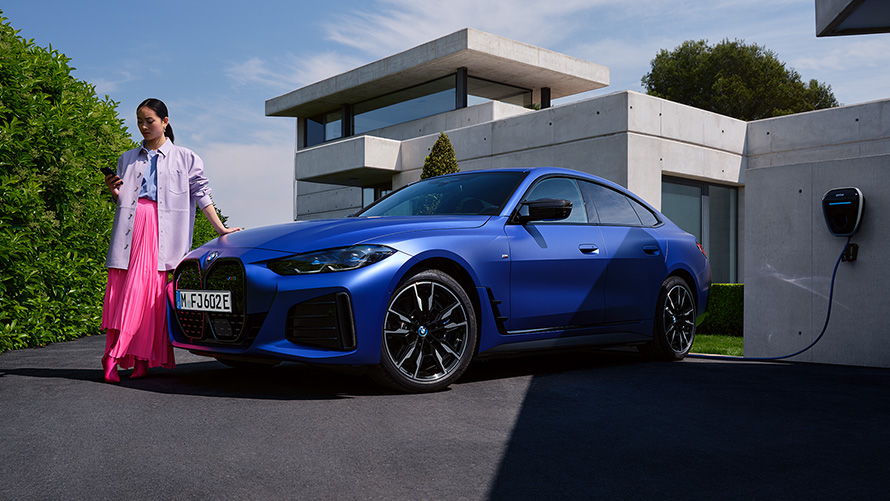 BMW i4 M50 G26 2021, BMW Individual Frozen Portimao Blue metallik, kolm neljandikku eestvaade, seismas maja ees koos naisega