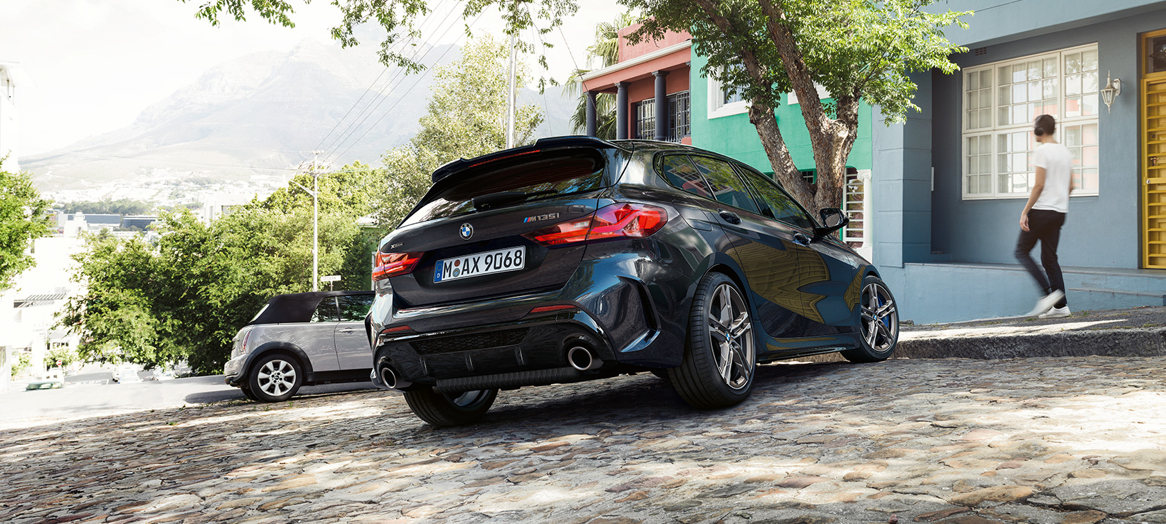 BMW M135i xDrive, kolm neljandikku tagantvaade. BMW M135i xDrive in Black Sapphire metallic, three-quarter rear view parking in front of a residential building.