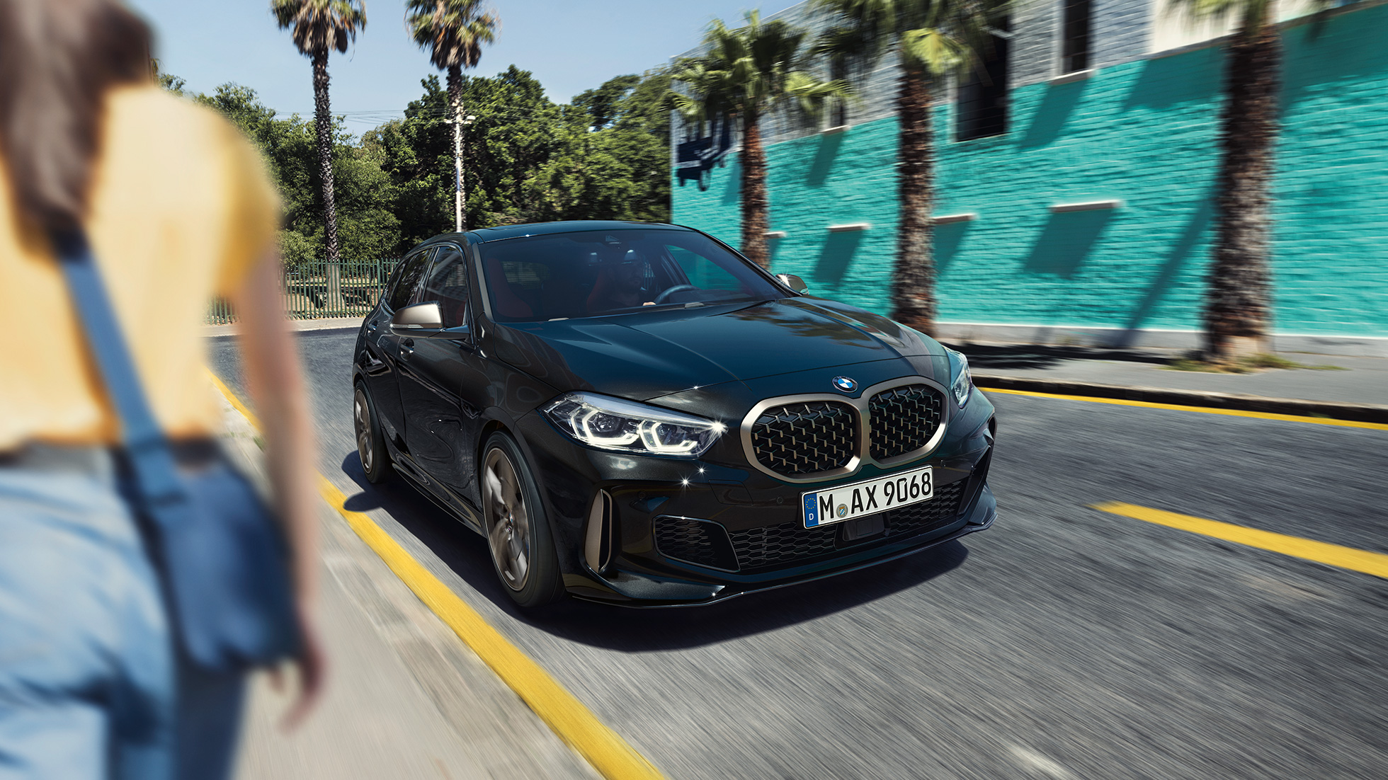BMW M135i xDrive, kolm neljandikku eestvaade. Uus BMW M135i xDrive toonis Black Sapphire metallik, kolm neljandikku eesvaatega sõites, koos naisega esiplaanil.