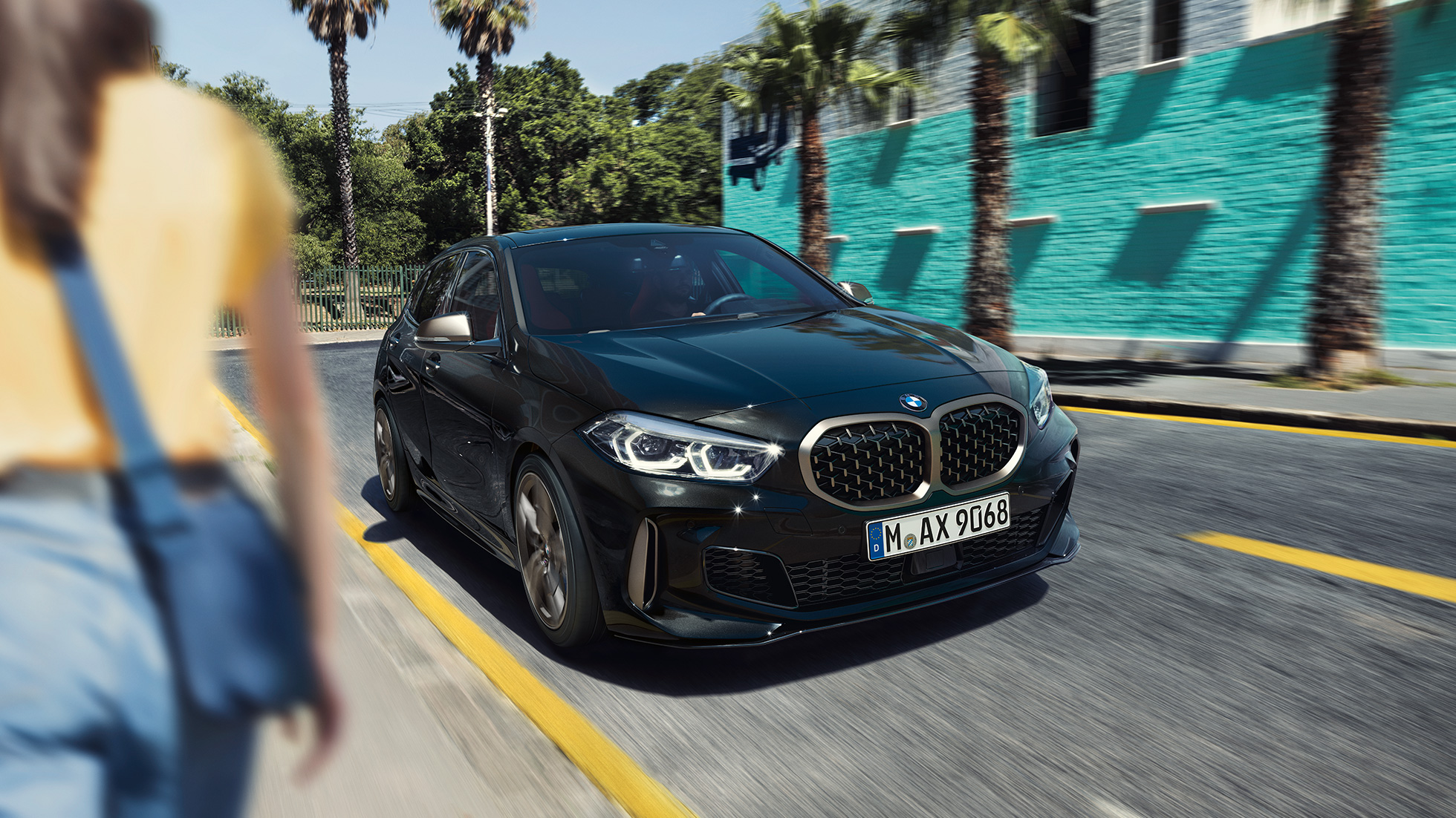 BMW M135i xDrive, kolm neljandikku eestvaade. Uus BMW M135i xDrive toonis Black Sapphire metallik, kolm neljandikku eesvaatega sõites, koos naisega esiplaanil.