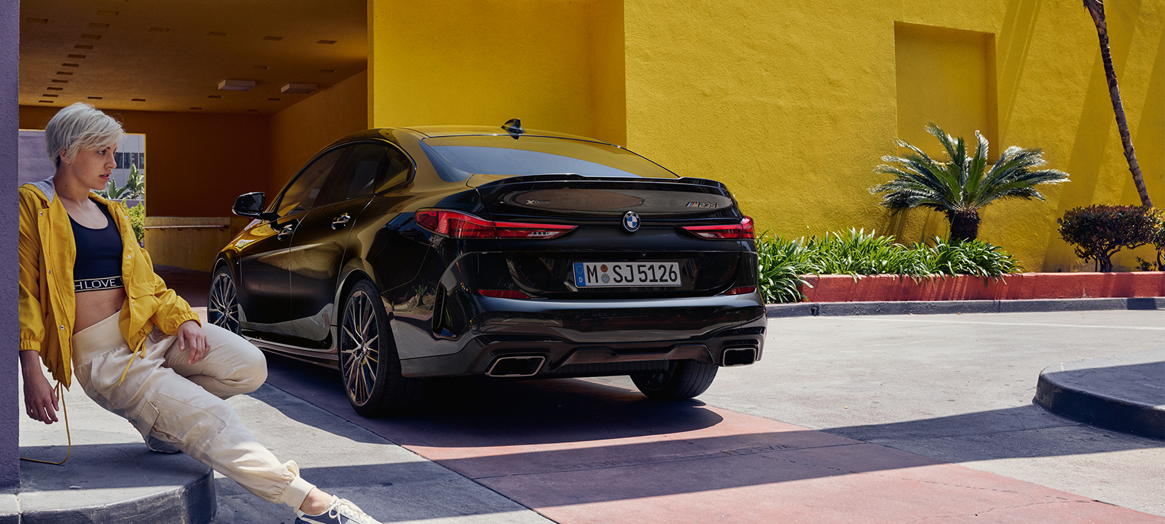 BMW M235i xDrive Gran Coupé kolm neljandikku tagantvaade BMW M235i xDrive Gran Coupé toonis Black Sapphire metallik F44 kolm neljandikku tagantvaade, naine esiplaanil
