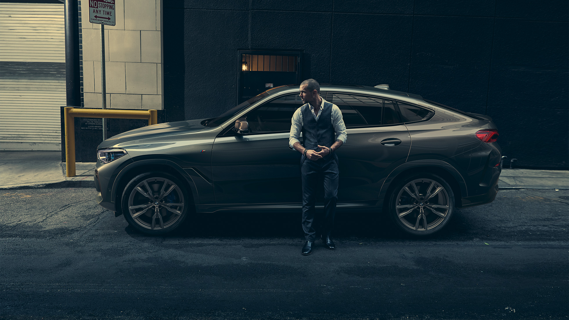 Man leaning on BMW X6 M50i in lateral perspective in front of an urban setting. Man leaning on BMW X6 M50i in lateral perspective in front of an urban setting.
