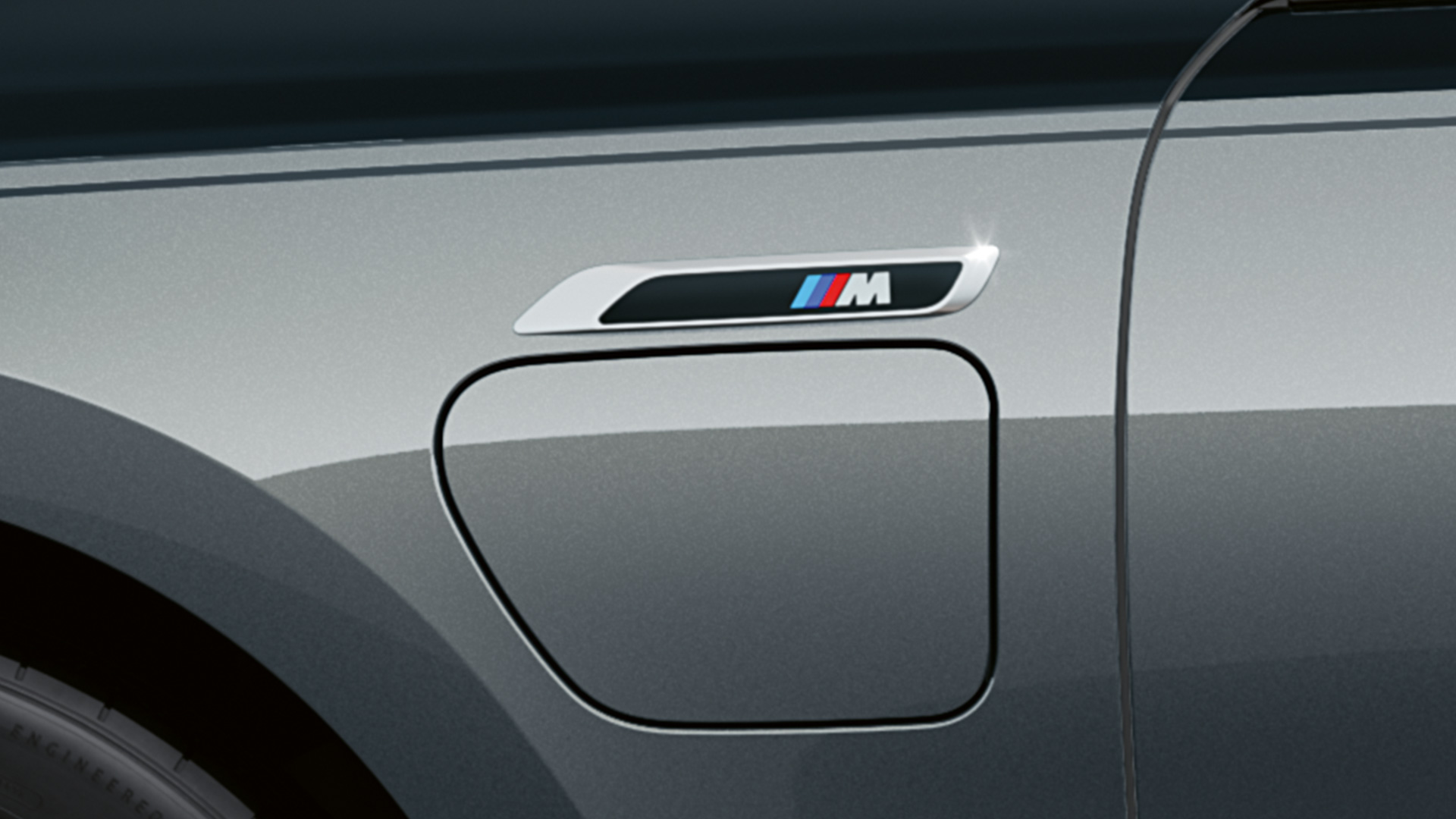 BMW M760e xDrive Sedaan G70, M-embleem BMW M760e xDrive Sedaan G70 M Performance‘i pakett BMW Individuali kahetooniline Black Sapphire metallik kerevärv, BMW Individuali Dravite Grey metallik, M-embleem, külgvaade lähedalt