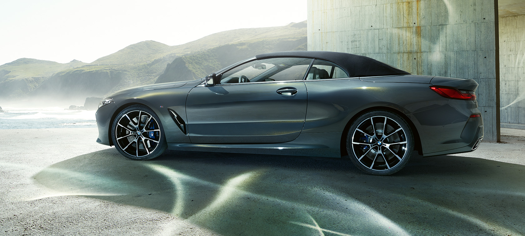 BMW M850i xDrive Cabrio, külgvaade. BMW M850i xDrive Cabrio toonis Dravit Grey metallik, suletud pehme katusega, külgvaade mägede taustal.