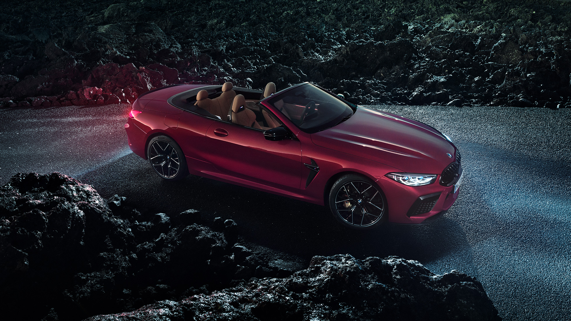 BMW M8 Competition Cabrio, kolm neljandikku külgvaade. BMW M8 Competition Cabrio toonis Motegi Red metallik, avatud pehme katusega, kolm neljandikku külgvaade, öösel asfaldil seismas.