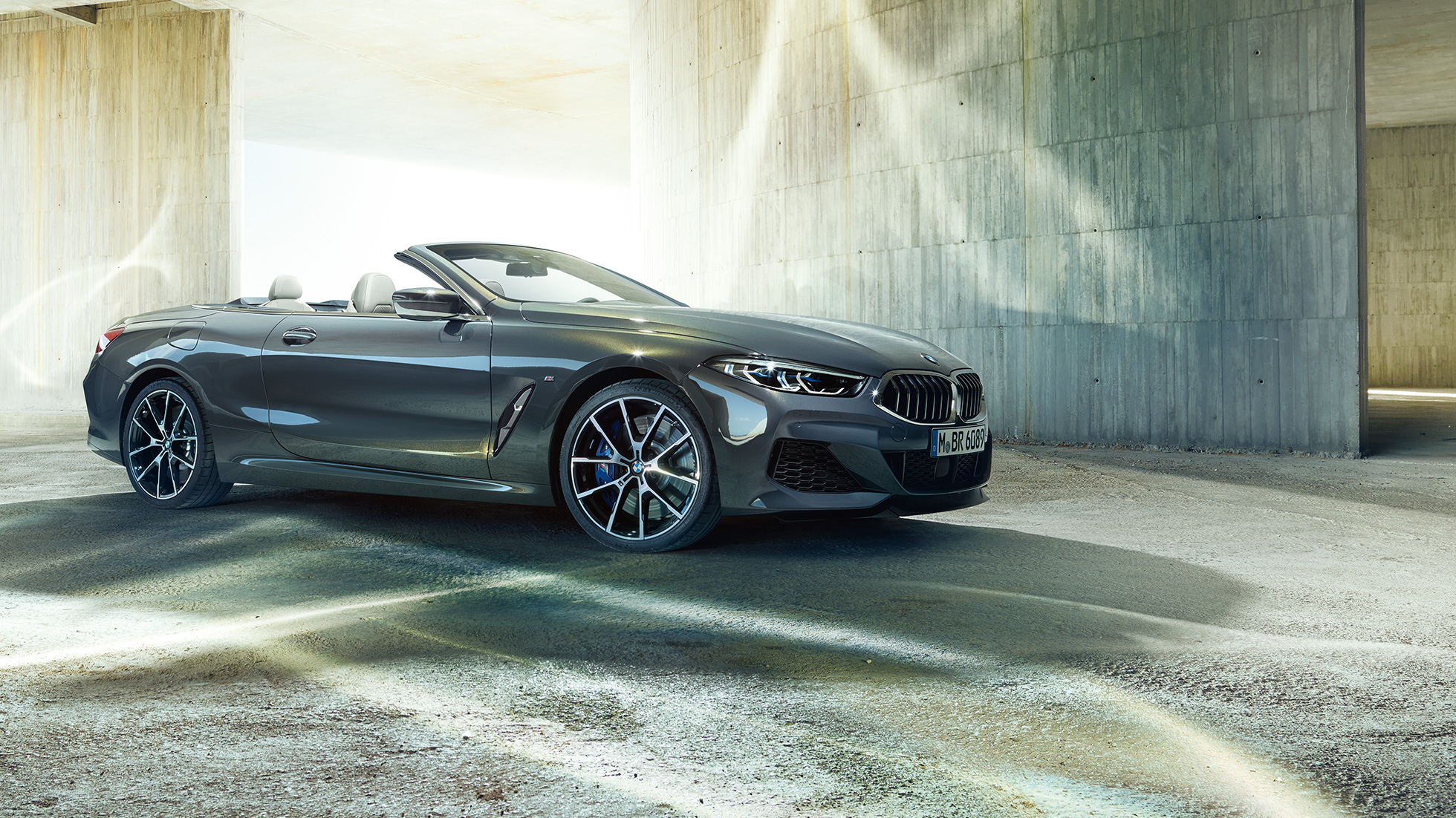 BMW M850i xDrive Cabrio, kolm neljandikku külgvaade. BMW M850i xDrive Cabrio toonis Dravit Grey metallik, avatud pehme katusega, kolm neljandikku külgvaade, seismas betoonehitise ees.