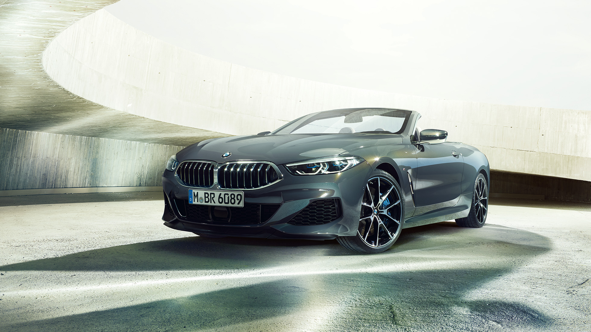 BMW M850i xDrive Cabrio, kolm neljandikku eestvaade. BMW M850i xDrive Cabrio toonis Dravit Grey metallik, avatud pehme katusega, kolm neljandikku eestvaade, seismas betoonehitises.