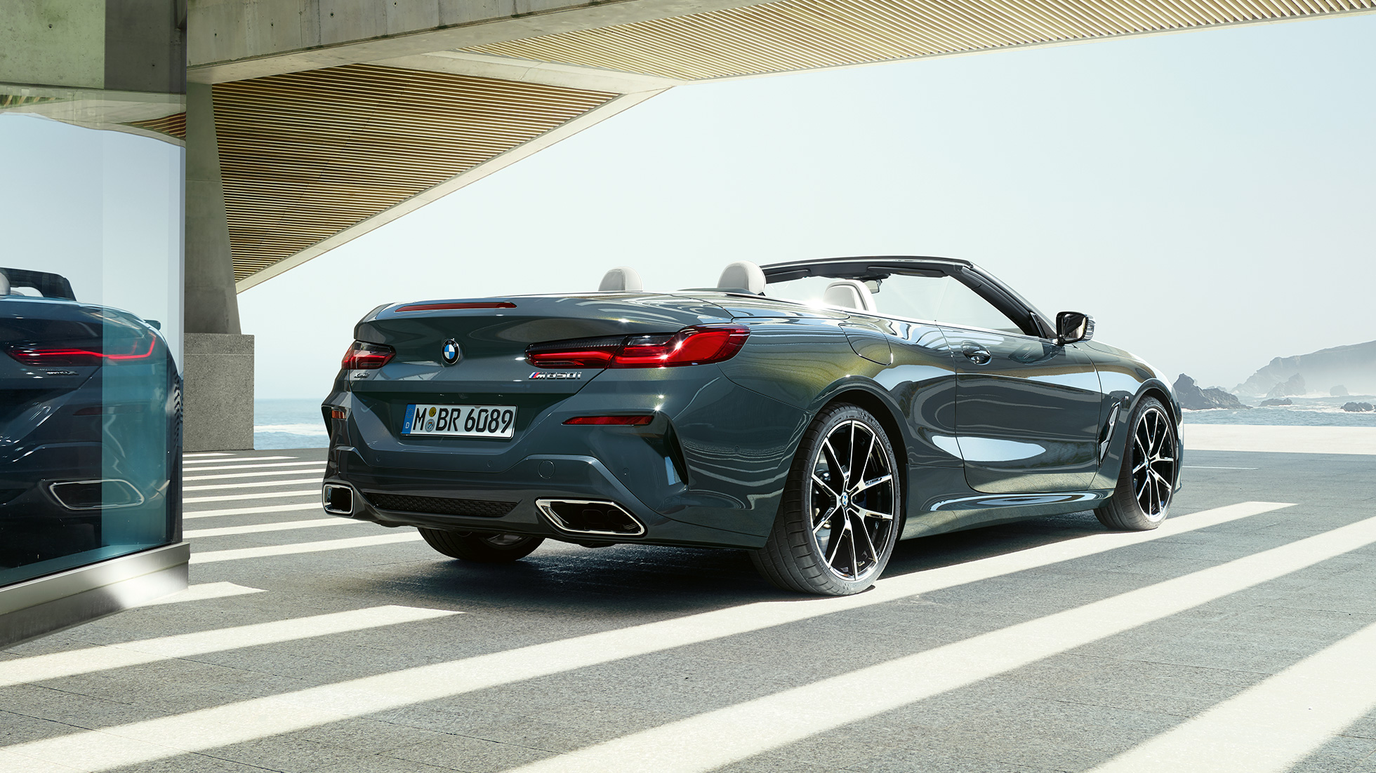 BMW M850i xDrive Cabrio, kolm neljandikku tagantvaade. BMW M850i xDrive Cabrio toonis Dravit Grey metallik, avatud pehme katusega, kolm neljandikku tagantvaade, parkimas vaatega ookeanile.