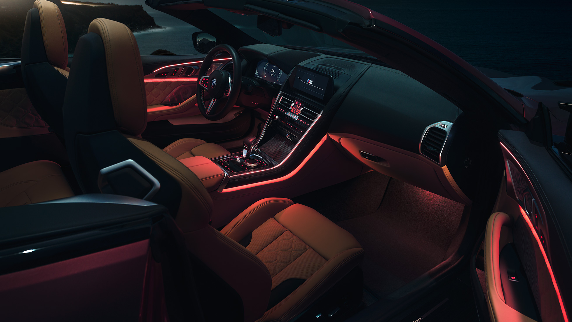 BMW M8 Competition Cabrio, salong. BMW M8 Competition Cabrio, avatud pehme katusega, salong punase salongivalgustusega öösel.