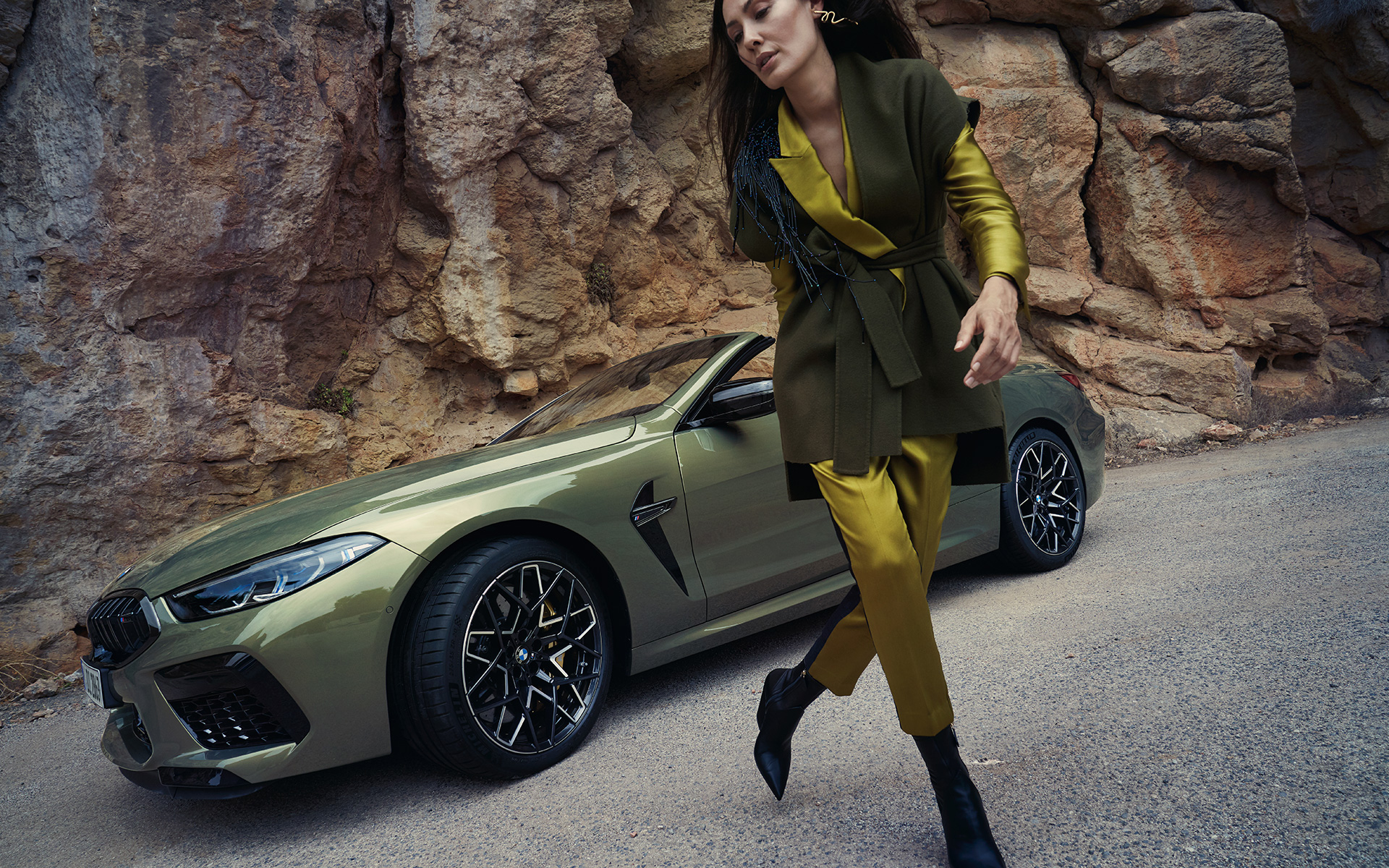 BMW M8 Competition Cabrio F91 LCI Facelift 2022 BMW Individual Brass metallik kolm neljandikku eestvaade seistes kivisel maastikul koos naismodelliga