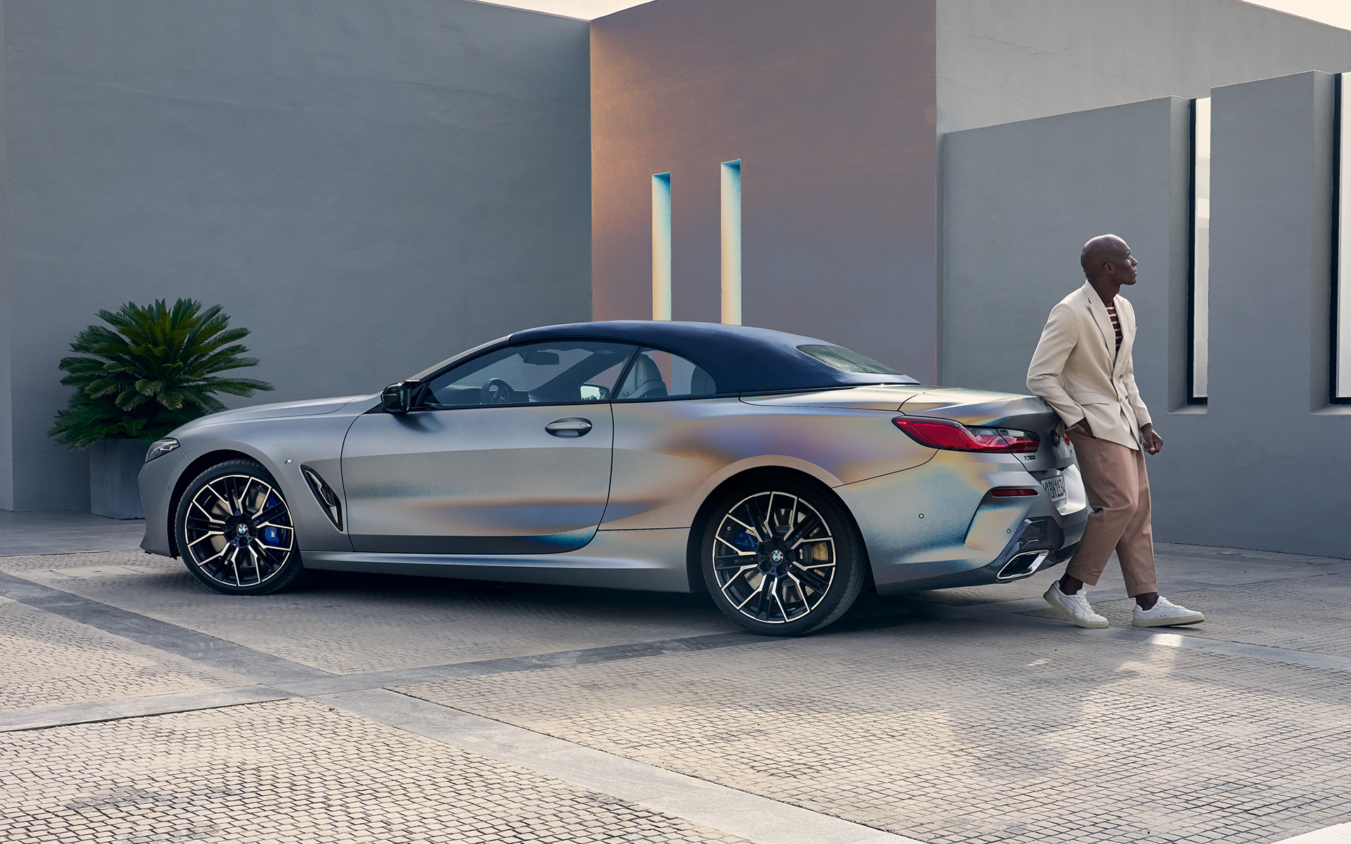 BMW M850i xDrive Cabrio G14 LCI Facelift 2022 BMW Individual Frozen Pure Grey metallik kolm neljandikku tagantvaade, meesmodell toetumas vastu sõidukit