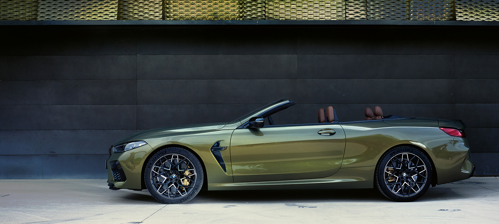 BMW M8 Competition Cabrio F91 LCI Facelift 2022 külgvaade seistes BMW M8 Competition Convertible F91 LCI Facelift 2022 BMW Individual Brass metallik külgvaade seistes avatud ukse ja naismodelliga