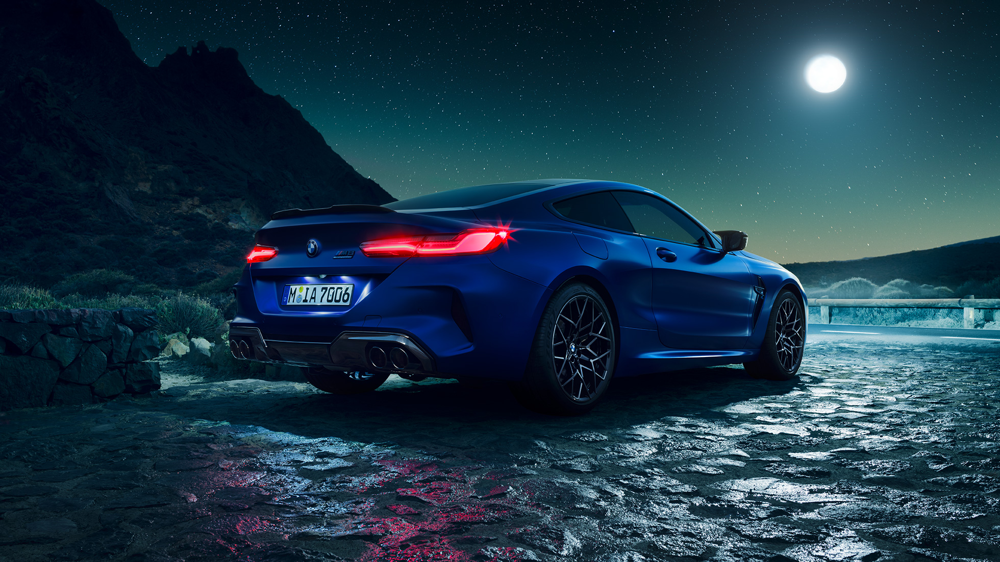 BMW M8 M Competition Coupé, kolm neljandikku tagantvaade. BMW M8 Competition Coupé toonis Marina Bay Blue metallik, põlevate LED-esituledega, kolm neljandikku tagantvaade, seismas täiskuuöös.