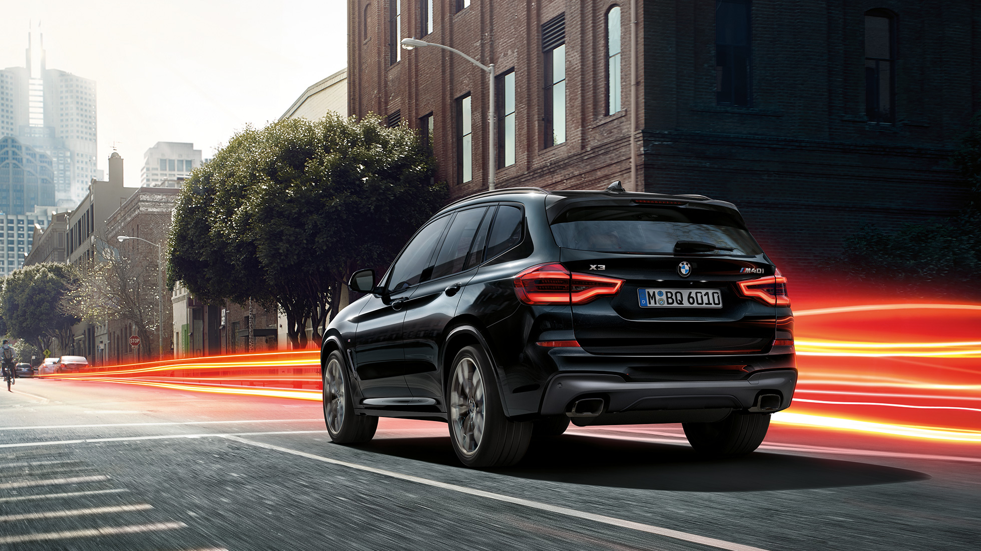 BMW X3 M40i, kolm neljandikku tagantvaade. Black Sapphire metallikvärvi BMW X3 M40i, sõitmas, välisilme, kolm neljandikku tagantvaade valgusribadega linnataustal.