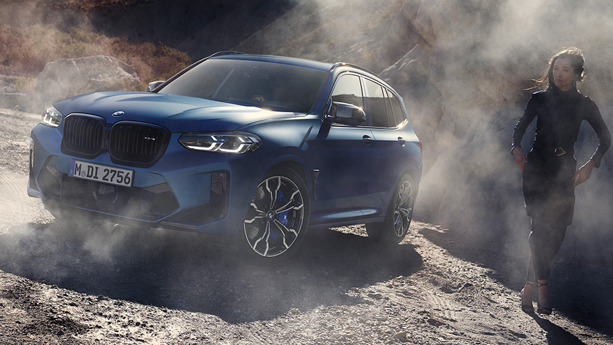 BMW X3 M Competition F97 LCI Facelift 2021, kolm neljandikku eestvaade seismas kivisel pinnasel BMW X3 M Competition F97 LCI Facelift 2021, toonis Frozen Marina Bay Blue metallik, kolm neljandikku eestvaade seismas kivisel pinnasel koos naismodelliga
