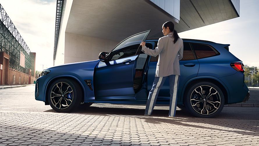 BMW X3 M Competition F97 LCI 2021, külgvaade avatud ukse ja naismodelliga BMW X3 M Competition F97 LCI Facelift 2021, toonis Frozen Marina Bay Blue metallik, külgvaade avatud ukse ja naismodelliga