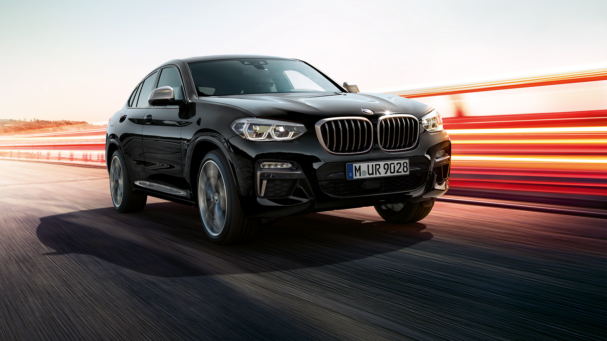 BMW X4 M40i ja BMW X4 M40d, kolm neljandikku eestvaade. Black Sapphire metallikvärvi BMW X4 M40i ja BMW X4 M40d, välisilme, kolm neljandikku vasakpoolne eestvaade valgusribadega.