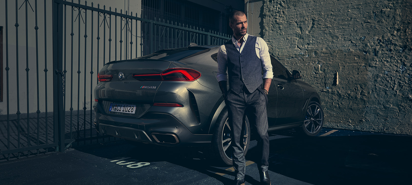 BMW X6 M50i kolm neljandikku tagantvaates, G06 Mees seismas kolm neljandikku tagantvaates BMW X6 M50i G06 2018 maasturi kõrval