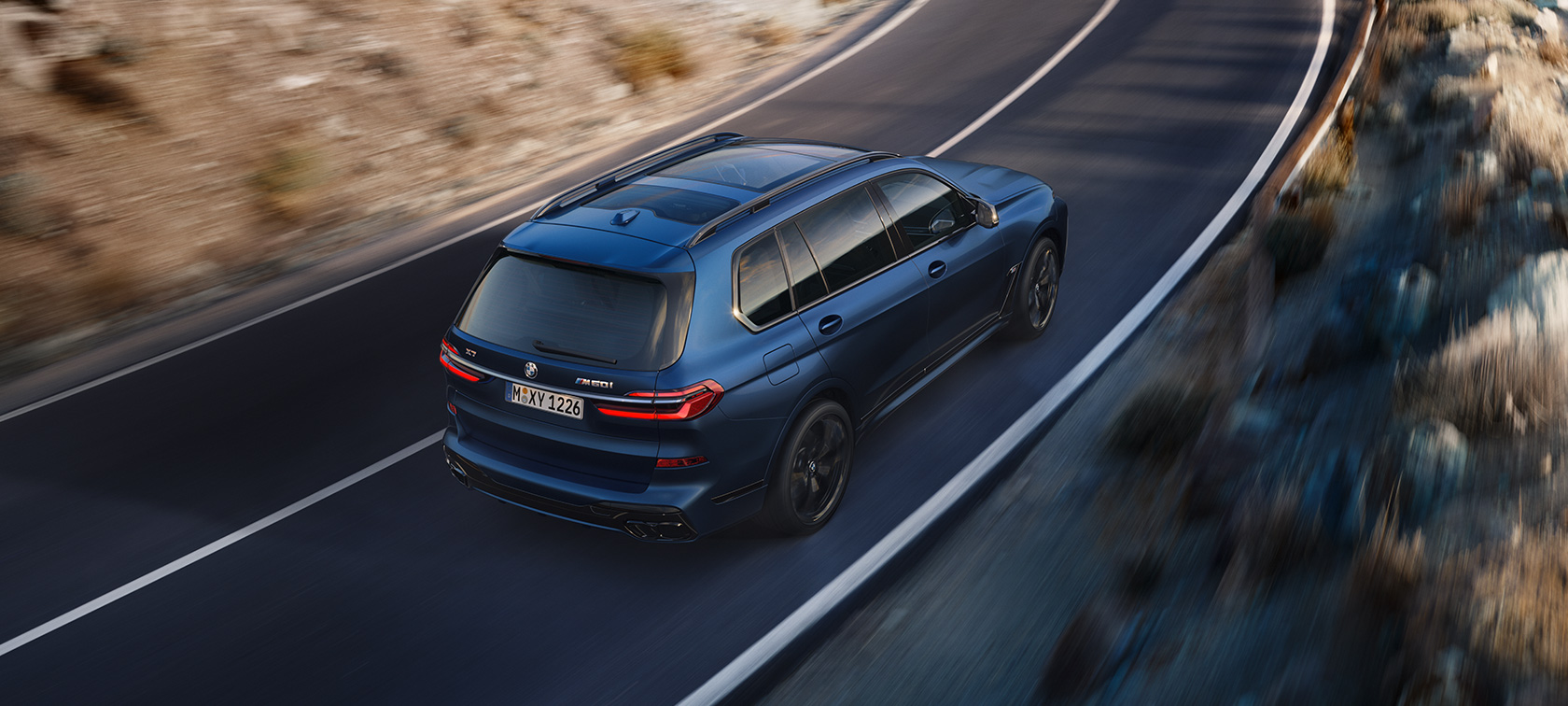 BMW X7 M60i G07 LCI, Frozen Marina Bay Blue, kolm neljandikku tagantvaade, ülaltvaade tänaval sõitmas