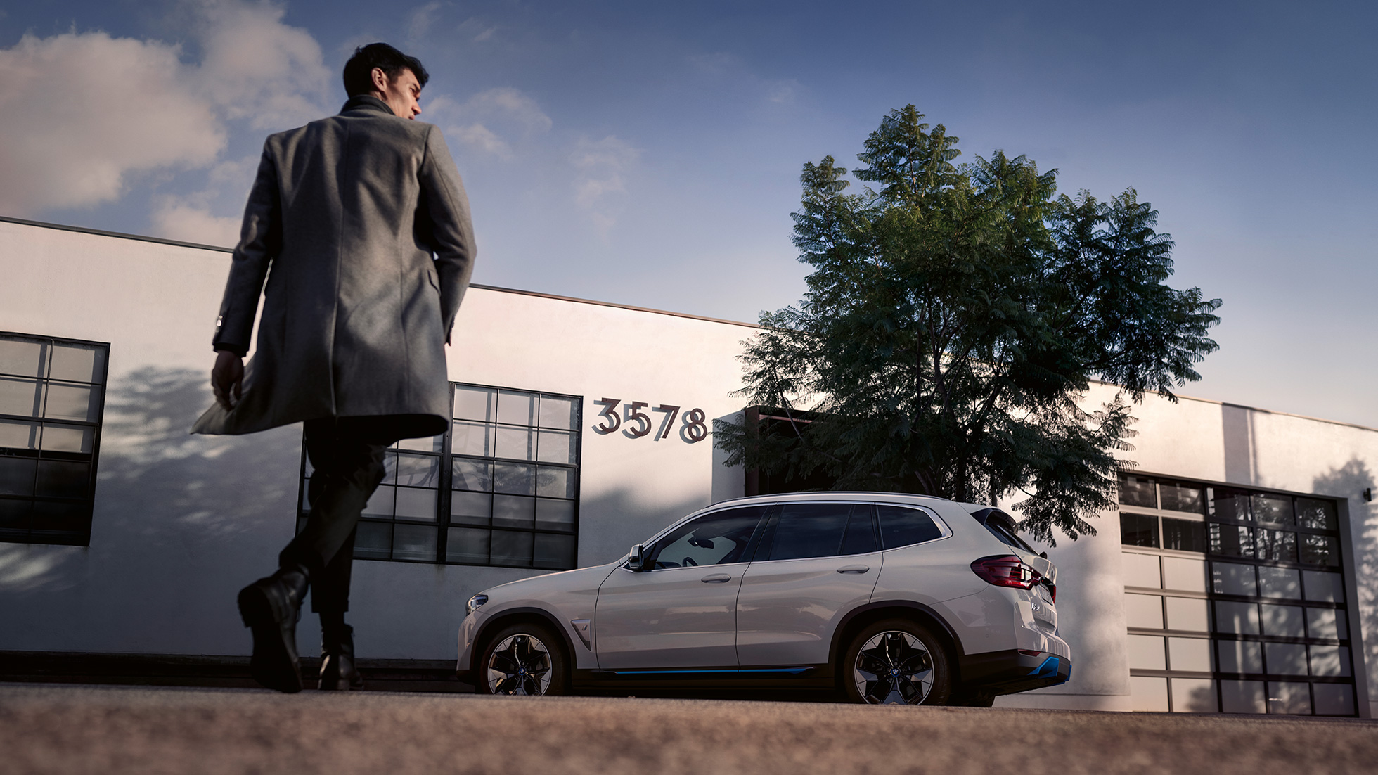 BMW iX3 G08 külgvaade hoone ees koos mehega BMW iX3 G08 2020 Mineral White metallik külgvaade hoone ees koos mehega
