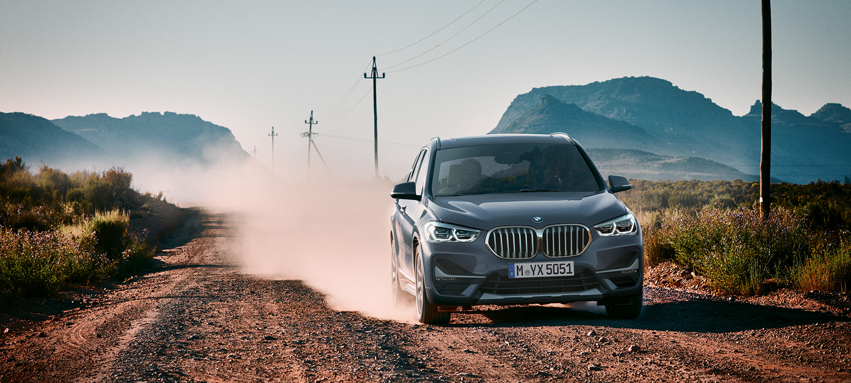 BMW X1, kolm neljandikku tagantvaade. BMW X1, kolm neljandikku tagantvaates sõitmas mäestiku taustal.