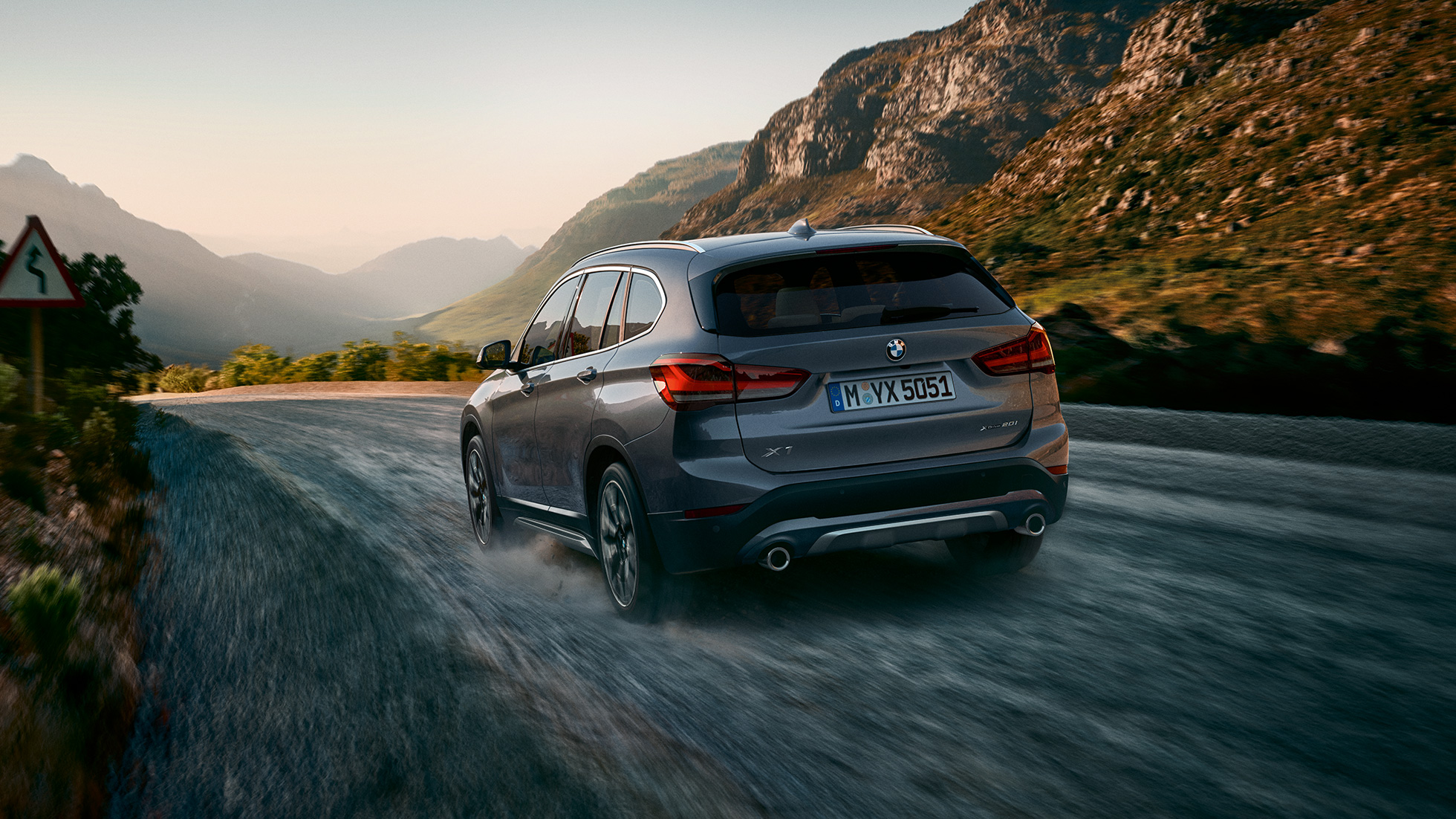 BMW X1, kolm neljandikku tagantvaade. BMW X1, kolm neljandikku tagantvaates sõitmas mäestiku taustal.