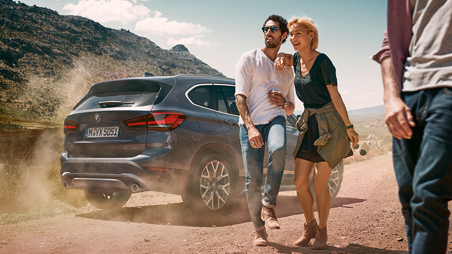 BMW X1 F48 LCI, Storm Bay, kolm neljandikku tagantvaade BMW X1 F48 LCI, Storm Bay, kolm neljandikku tagantvaade, sõitmas inimestega maastiku taustal