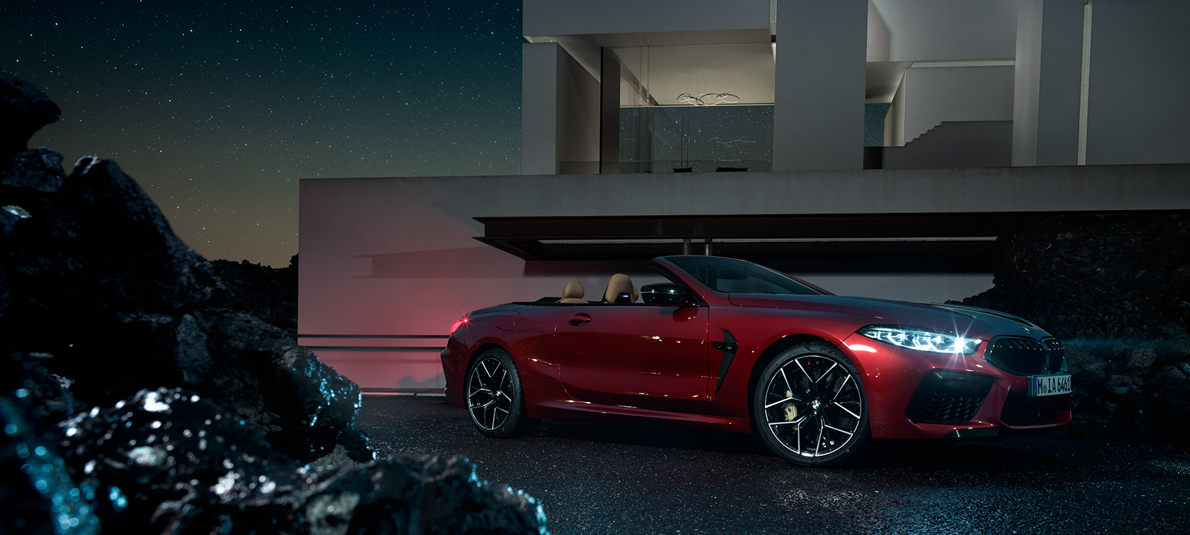 BMW M8 Competition Cabrio, kolm neljandikku külgvaates. BMW M8 Competition Cabrio toonis Motegi Red metallik, kolm neljandikku külgvaates, öösel villa ees seismas.