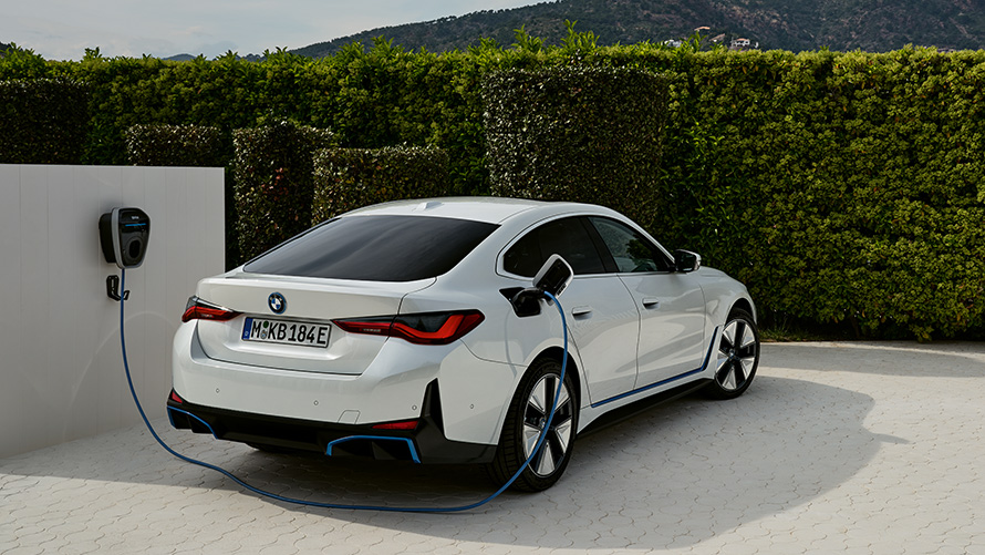Laadimine 3. põlvkonna BMW Wallboxiga, BMW i4 G26 elektriauto, kolm neljandikku tagantvaade BMW i4 G26 elektriauto, kolm neljandikku tagantvaade laadimas, ühendatud 3. põlvkonna BMW Wallboxi külge heki ees