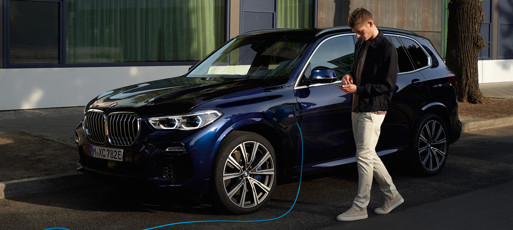 Mees kasutamas My BMW rakendust nutitelefonis Mees kasutamas BMW ConnectedDrive’i My BMW rakendust nutitelefonis BMW X5 pistikhübriidi laadimise ajal