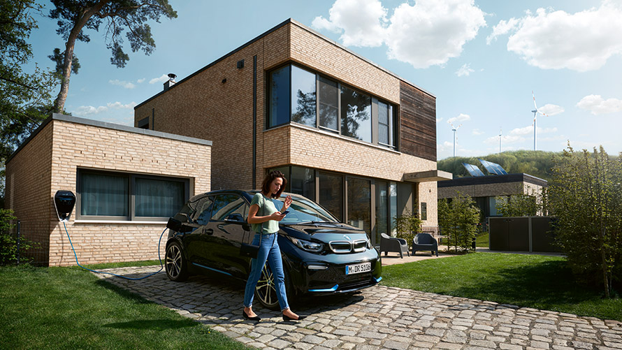 Digital Charging Service Naine kõnnib väljas BMW i3 ees ja kasutab oma nutitelefonil digitaalset laadimisteenust