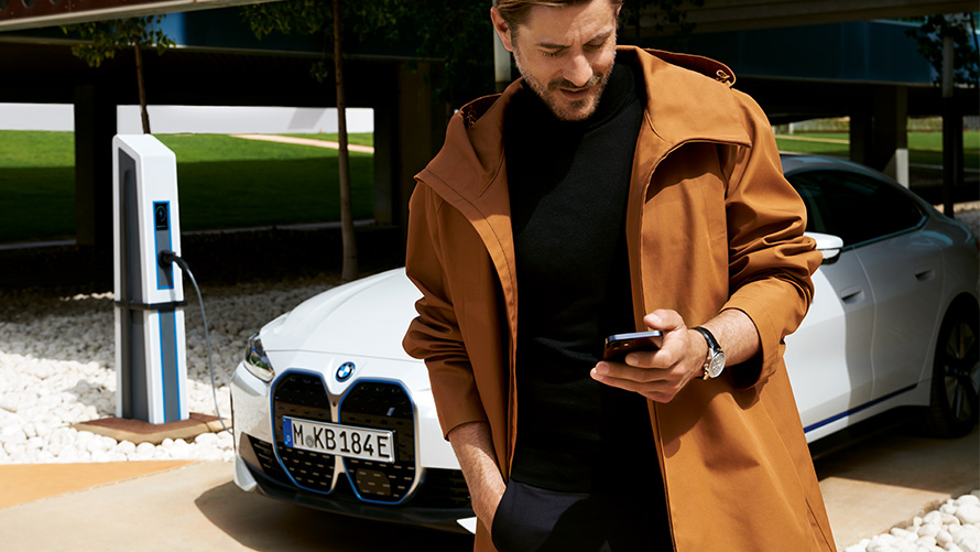BMW Service Inclusive’i kestus ja lepinguperioodid elektriautodele BMW Service Inclusive, mees vaatab laadimisjaamas BMW i4 ees nutitelefoni