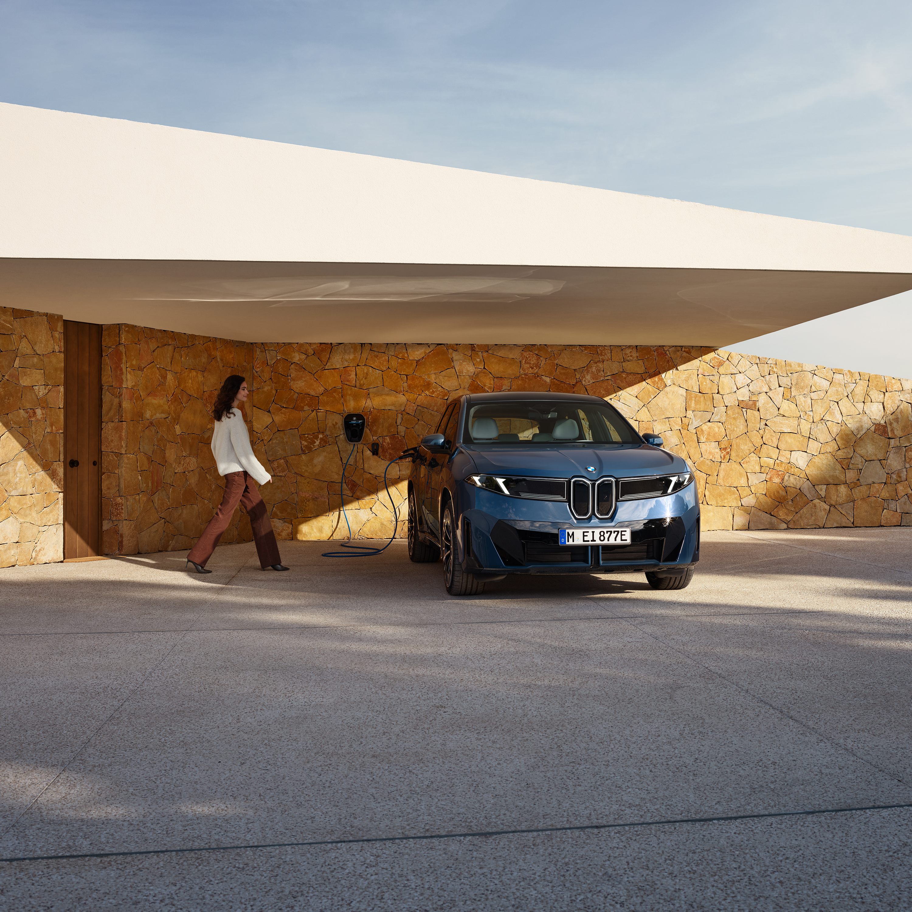 Naine kõnnib Wallboxiga ühendatud BMW iX3 poole